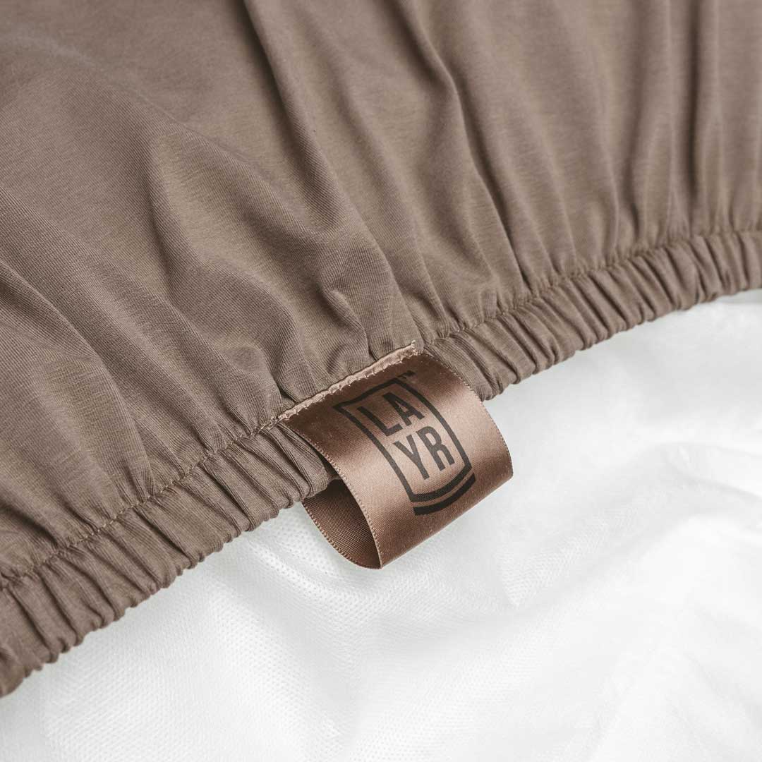 Close-up of brown dog bed cover with elastic band a visible LAYR brand label.