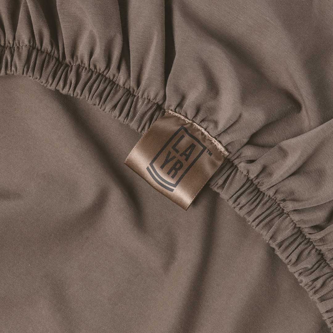 Close-up of brown dog bed cover with elastic band a visible LAYR brand label.